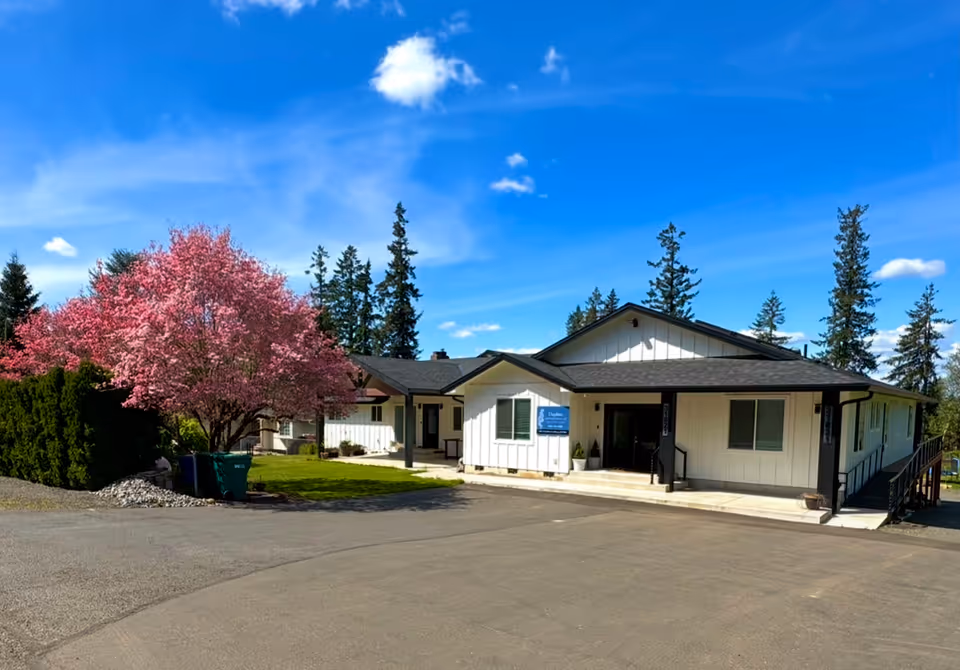 White single-story senior care building with pink blossoming tree and blue sky.