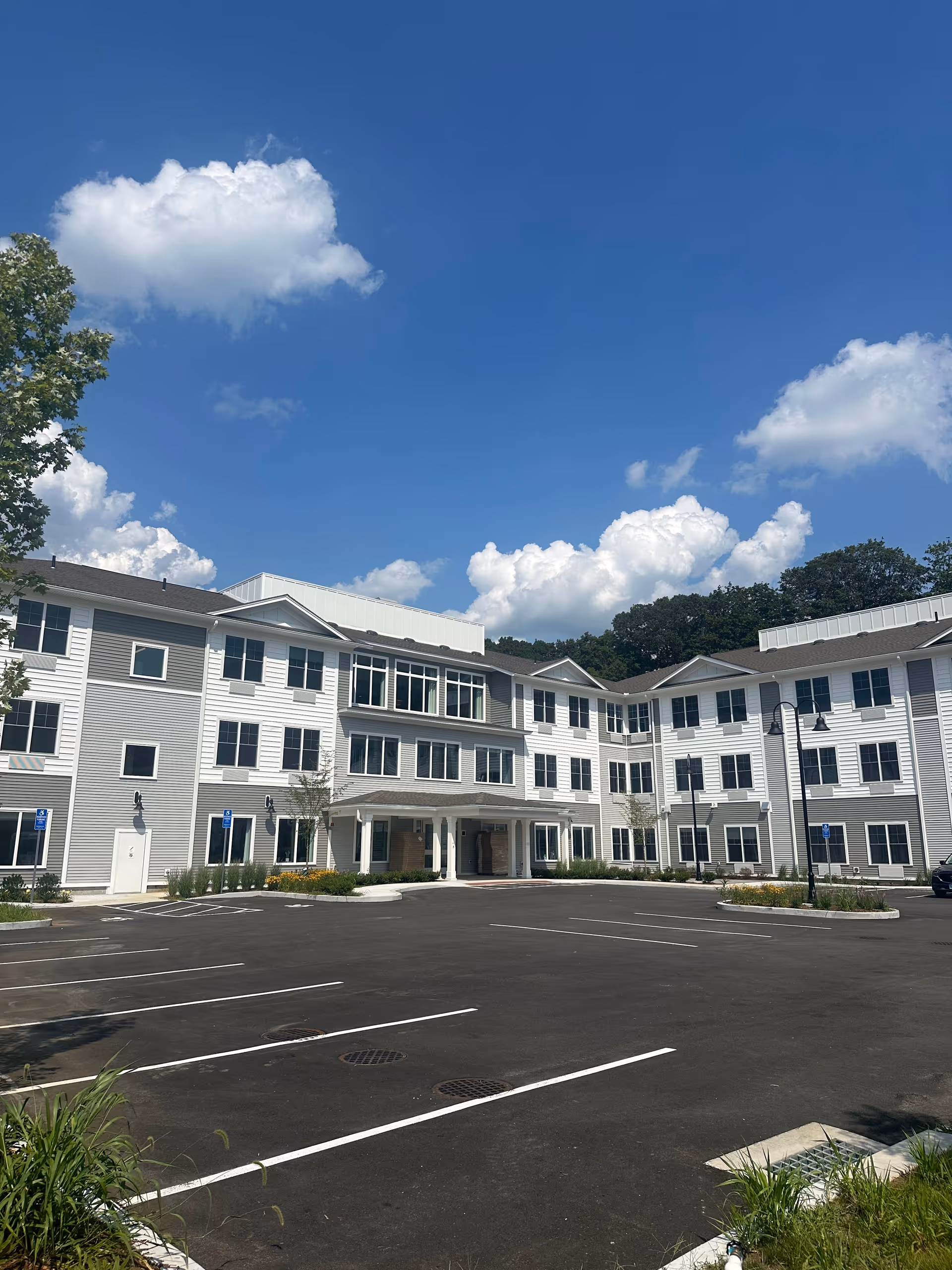 Exterior view of a KindCare Naugatuck senior living building with white siding and parking.
