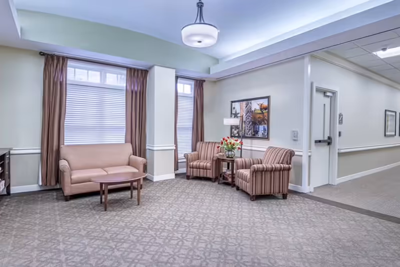 Senior living lobby with pink striped chairs, a sofa, coffee table, and floral arrangement.