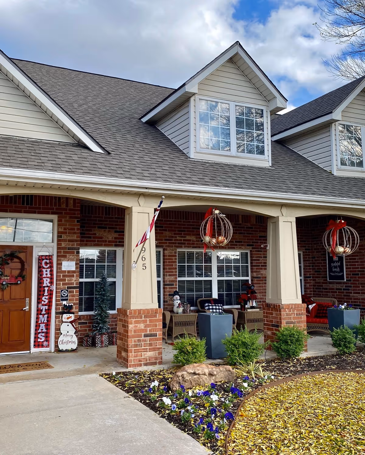 Senior living facility front porch decorated for Christmas with wreaths, chairs, and planters.
