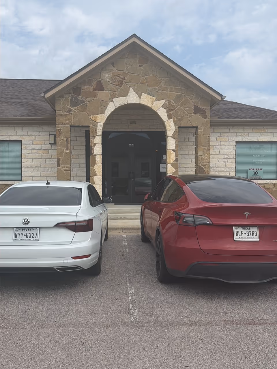 Stone-facade senior facility with arched entry and two parked cars in front.