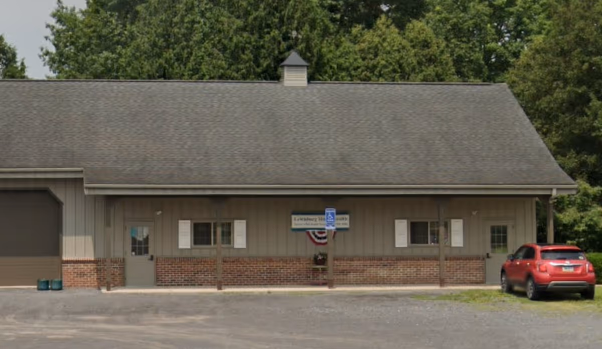 Single-story facility exterior with a covered front porch, center sign, and a red car nearby.