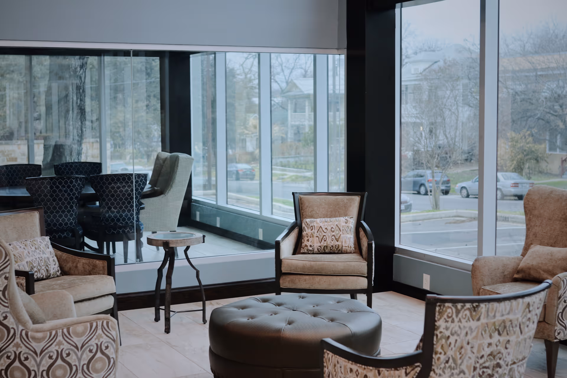 Cozy indoor lounge with upholstered chairs, an ottoman, and large windows.