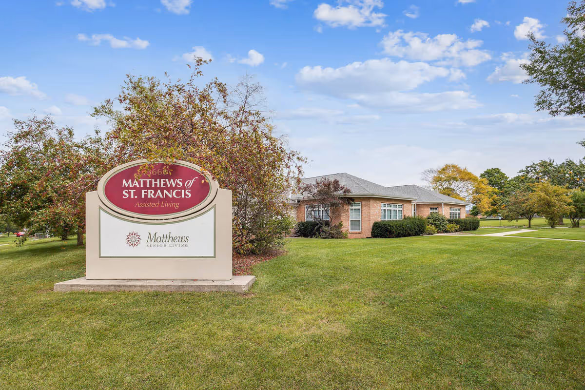 Sign reads Matthews of St. Francis Assisted Living near a brick building on a green lawn