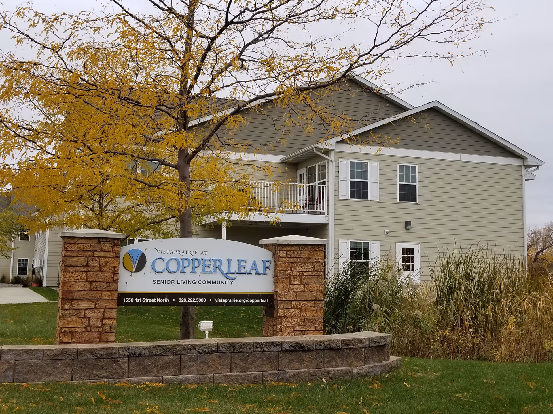 Two-story Vista Prairie at Copperleaf senior living building with sign in a landscaped yard