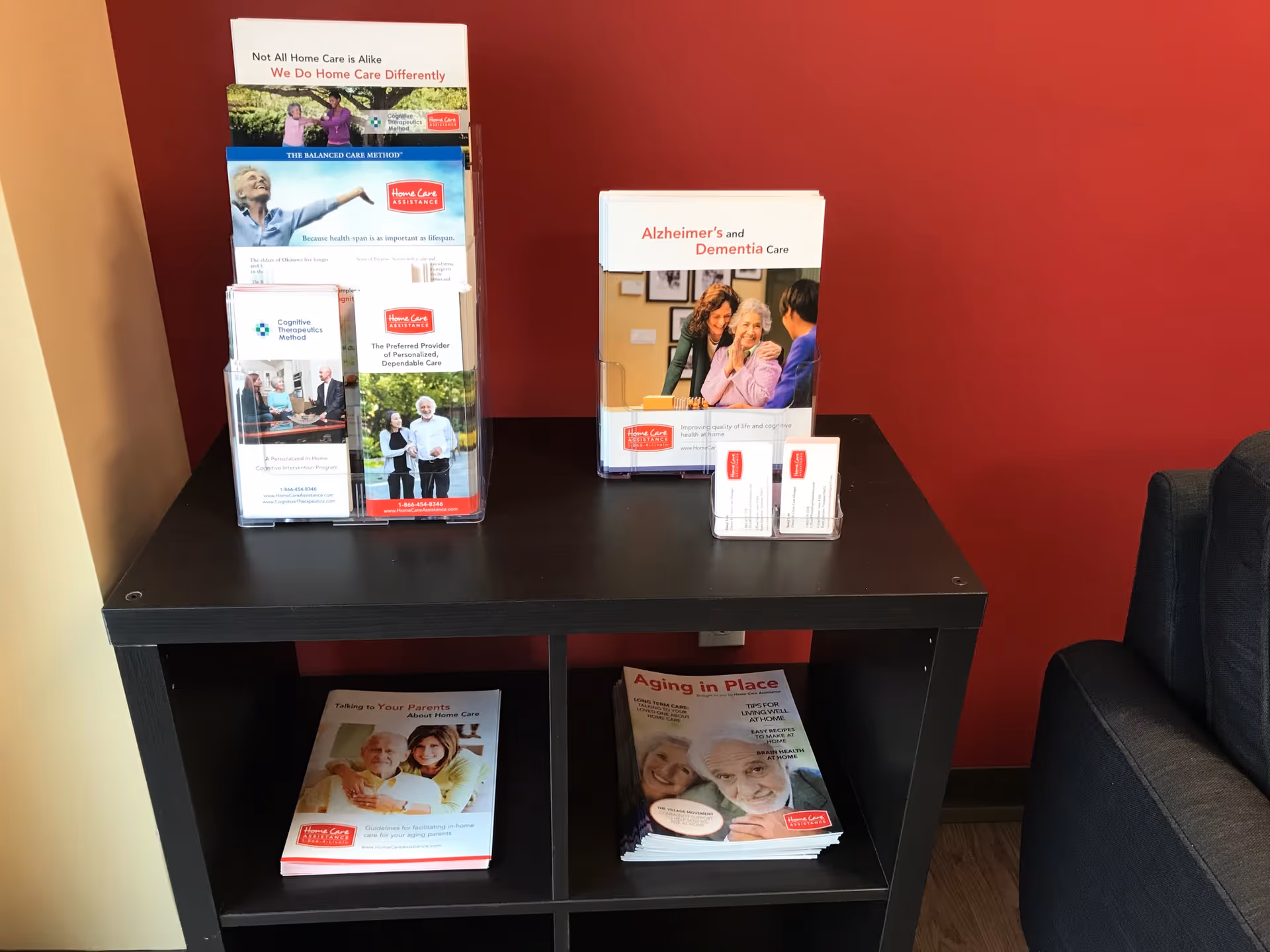 Black shelving unit holds brochures and magazines against red wall.