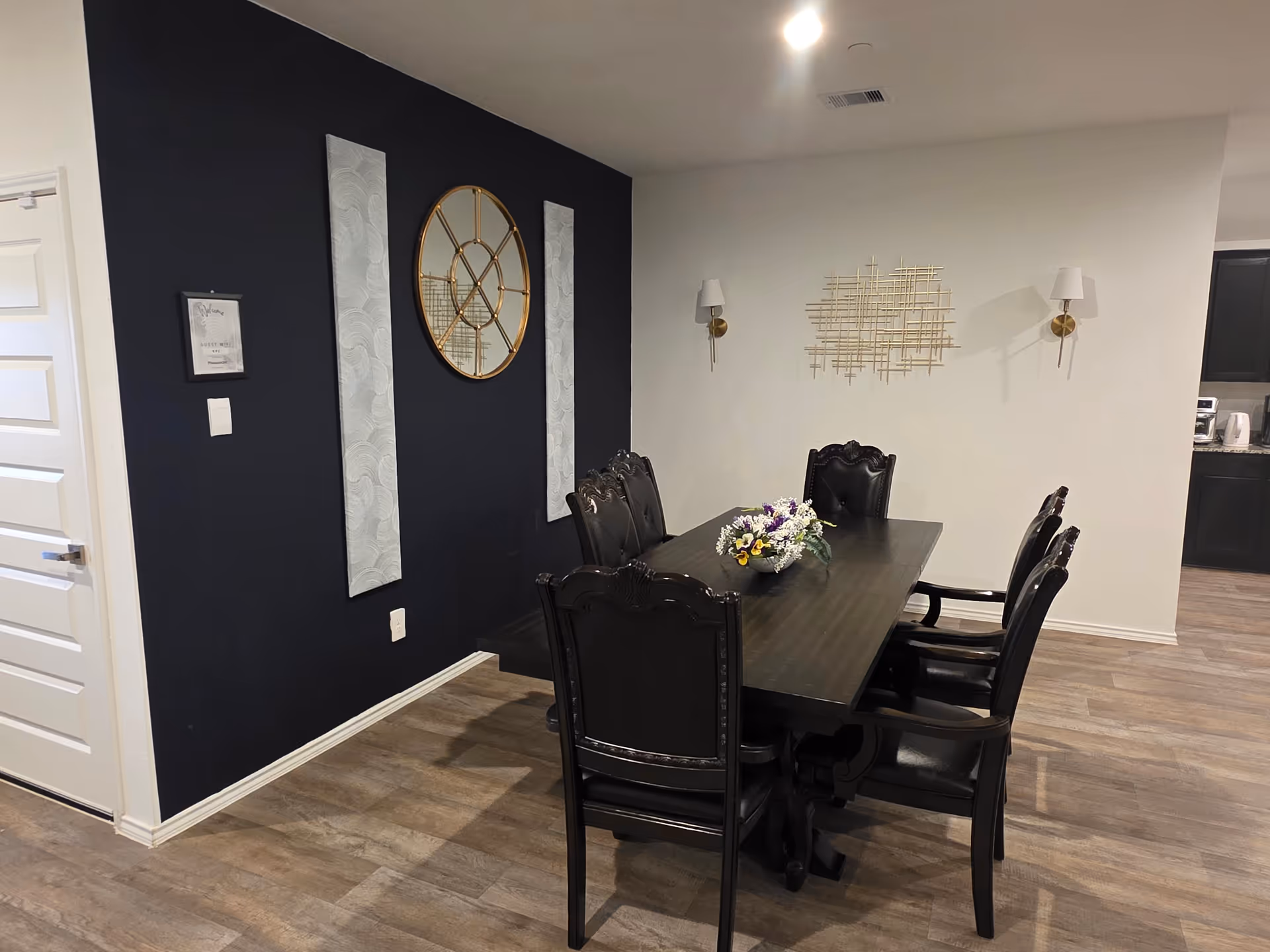 A dining room with a dark table, black chairs, wall decor, and floral centerpiece.