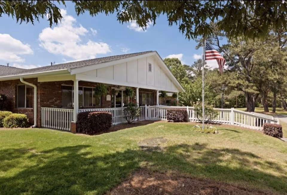 Front exterior of a single-story senior care facility with porch and flag.