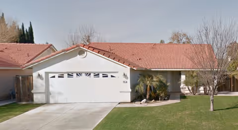 Front view of a single-story residence with a white garage door and red-tiled roof.