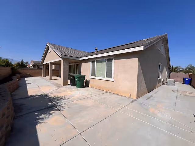 Exterior view of Bliss Homes building with beige walls, wide driveway, and trash bins.