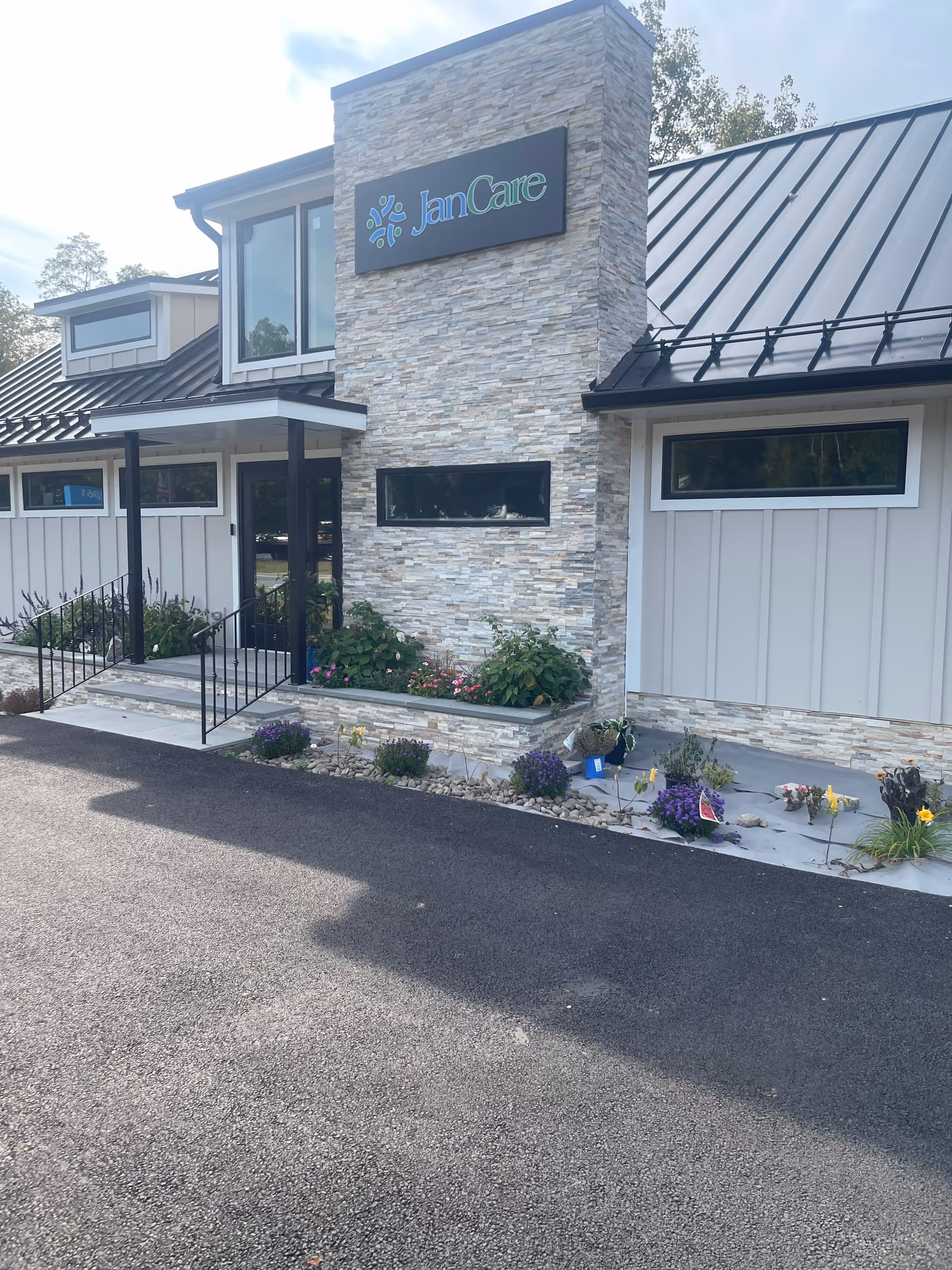 Exterior view of a JanCare facility with stone facade, sign, and landscaped entrance.