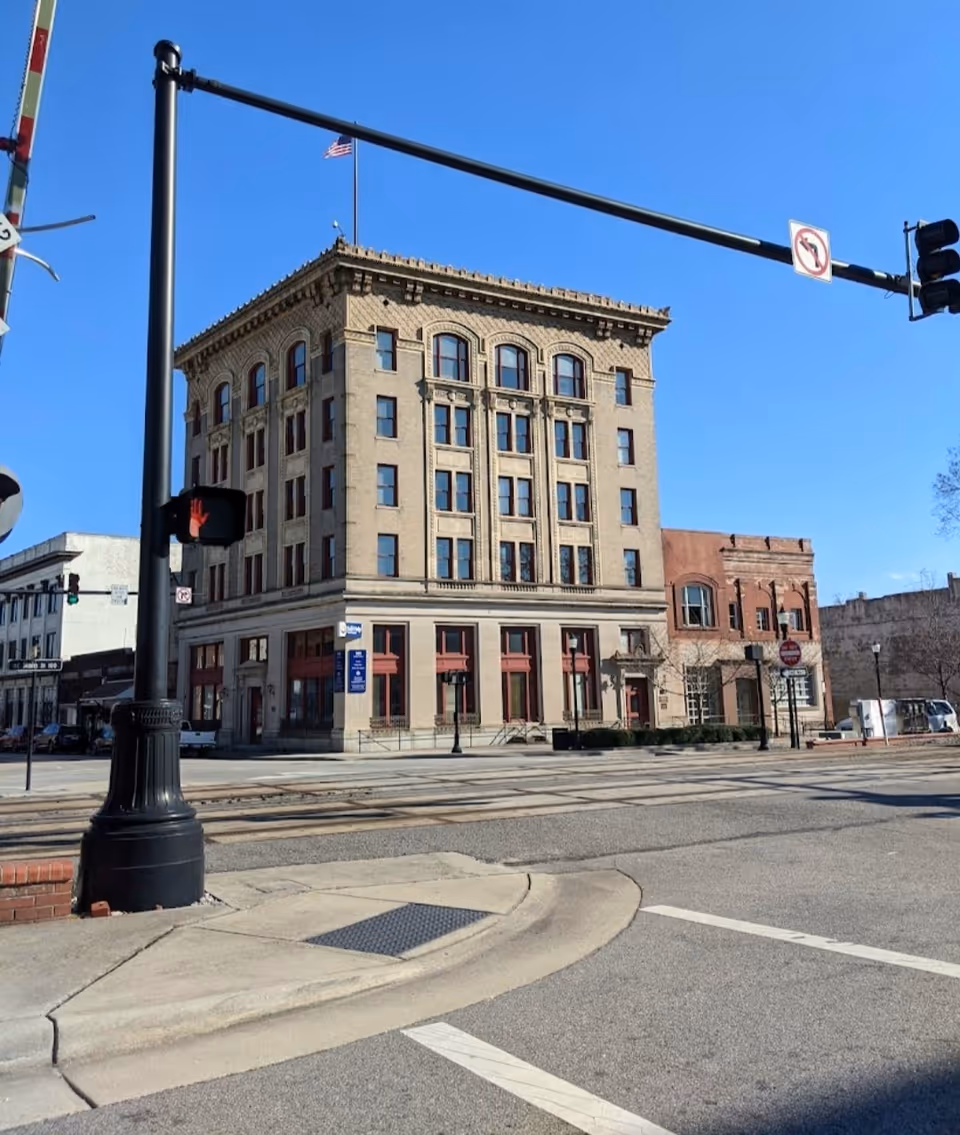Tall historic brick building on a sunny street corner with traffic signals.