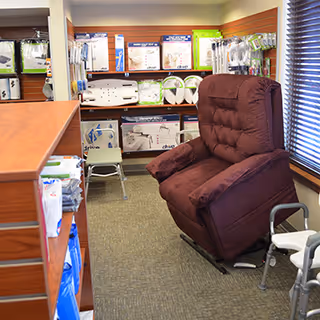 A burgundy reclining chair sits in a small showroom with medical supplies on shelves.