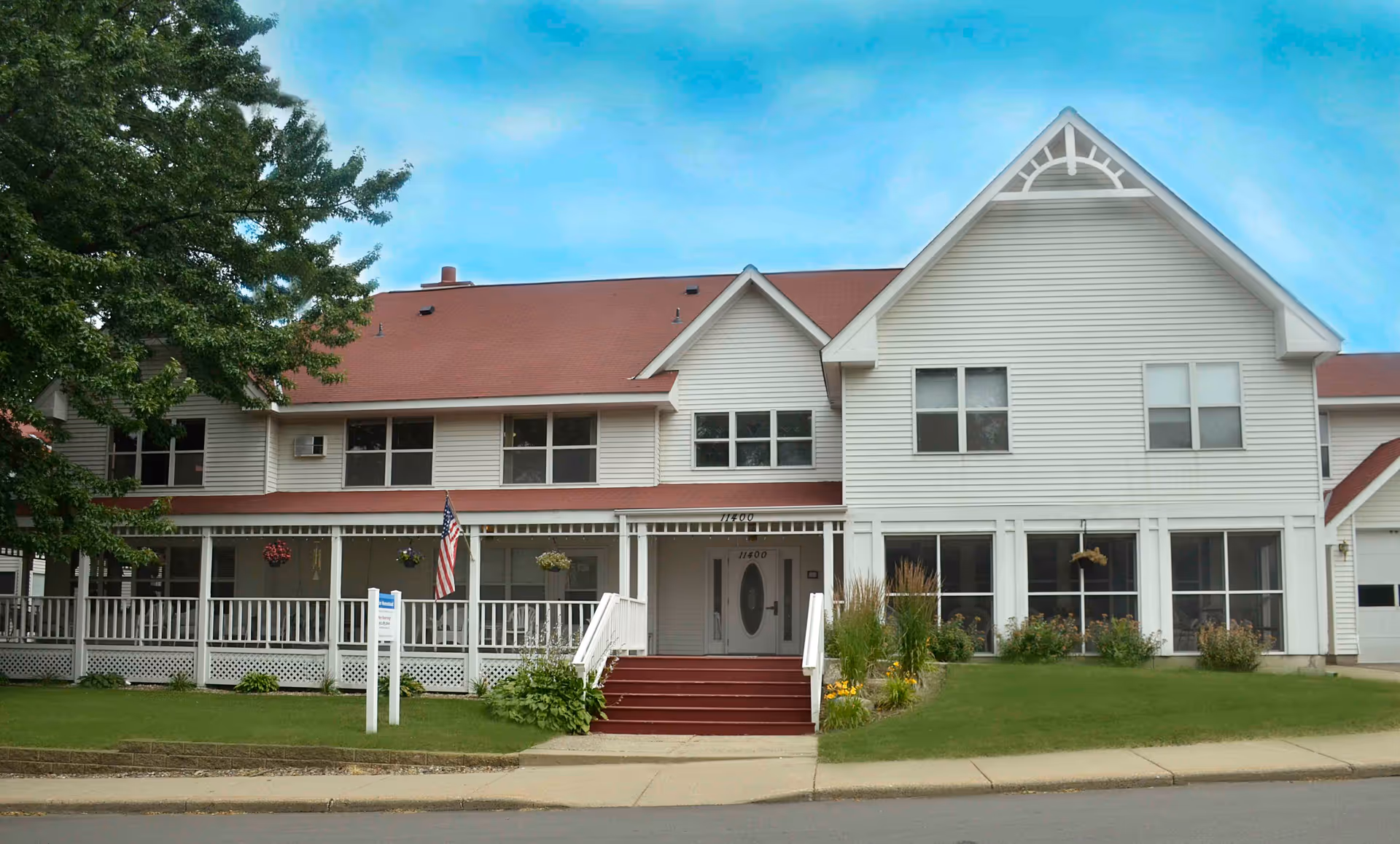 Exterior view of Elder Homestead senior living facility with a long porch, steps, and landscaped lawn.