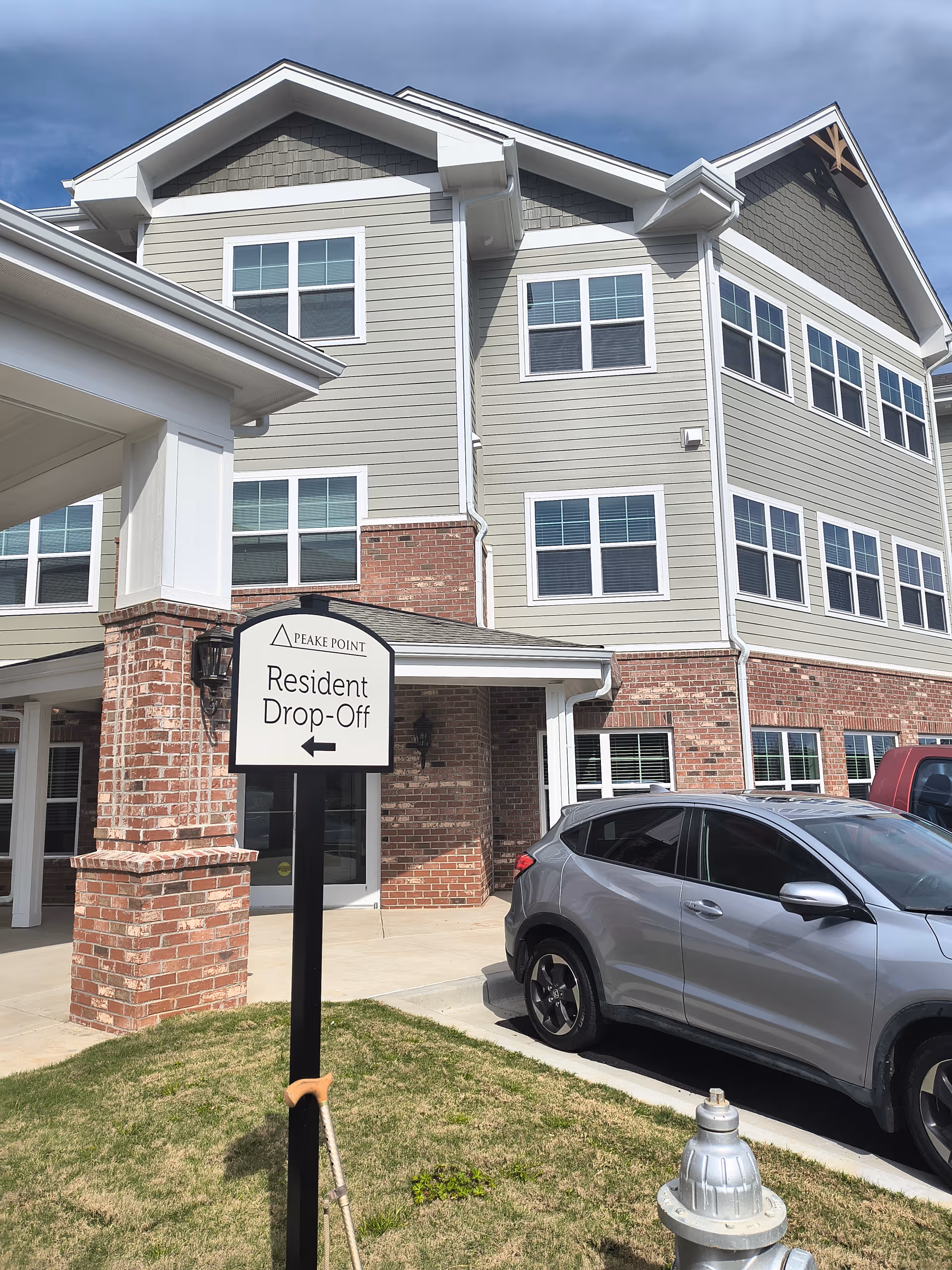 Exterior view of a senior living building with a drop off sign and a parked car.