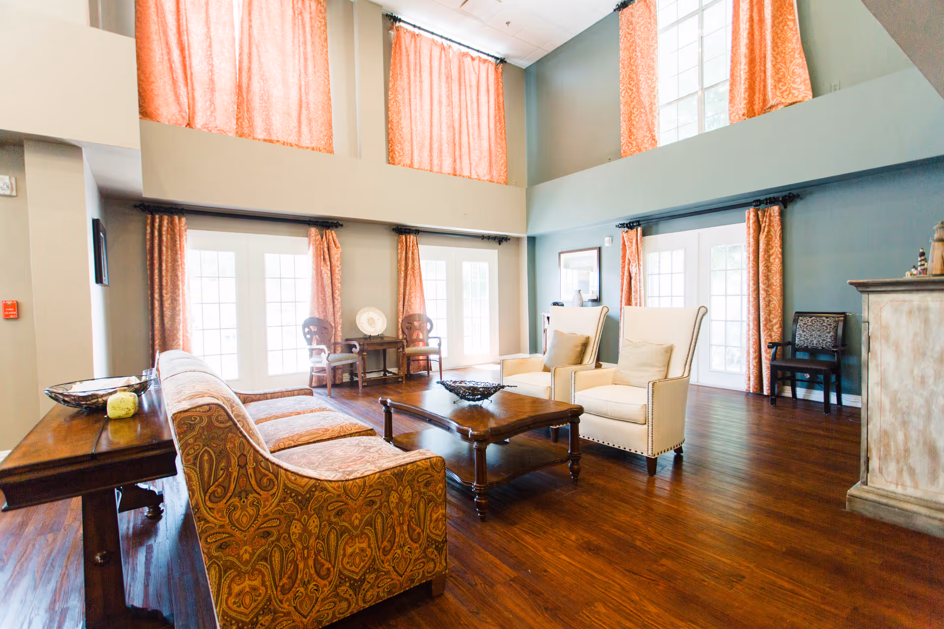 Spacious lounge area with sofas, chairs, and a coffee table in a senior living common room.