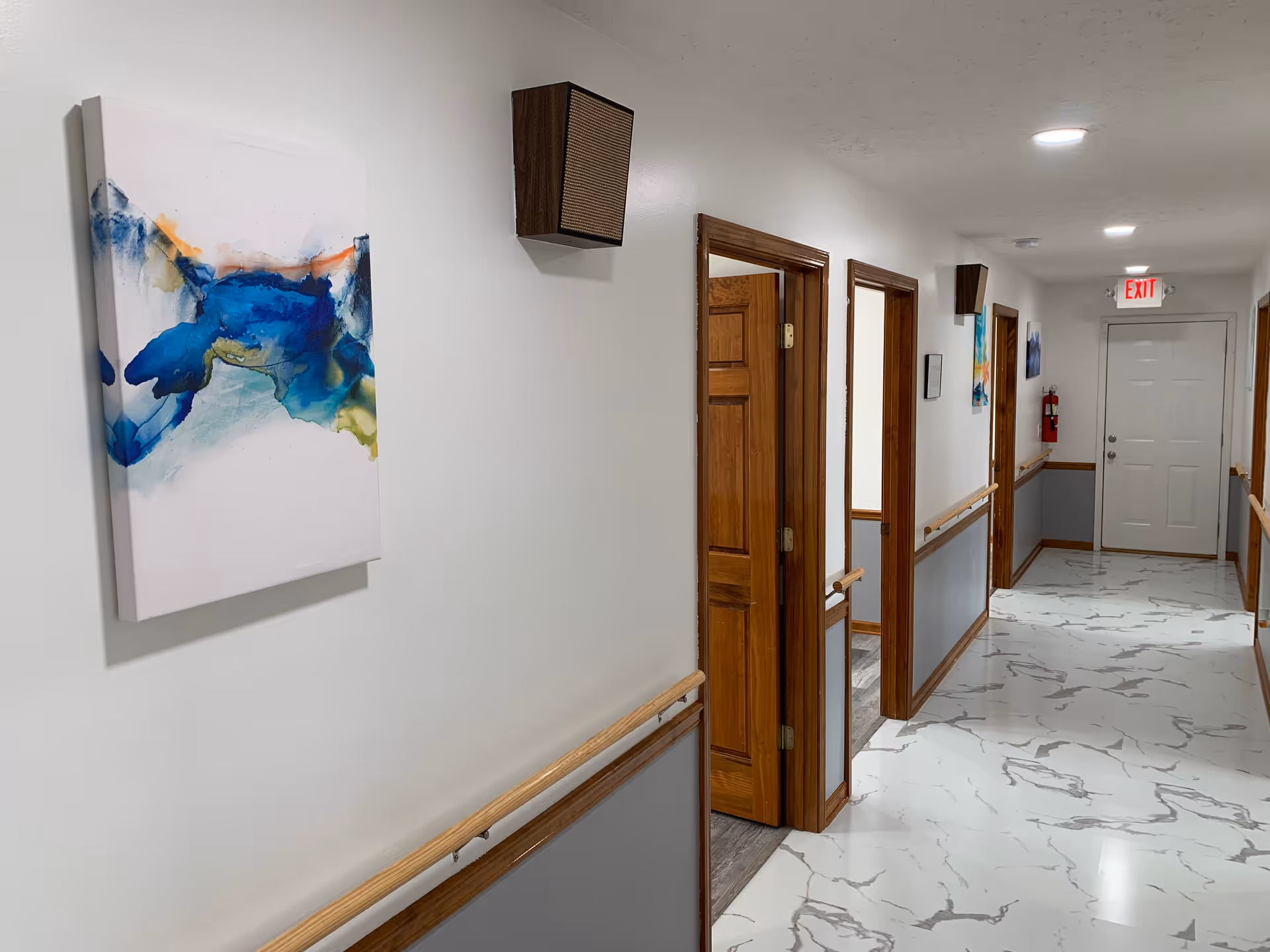 Interior hallway in a senior living facility with wooden doors and abstract art.