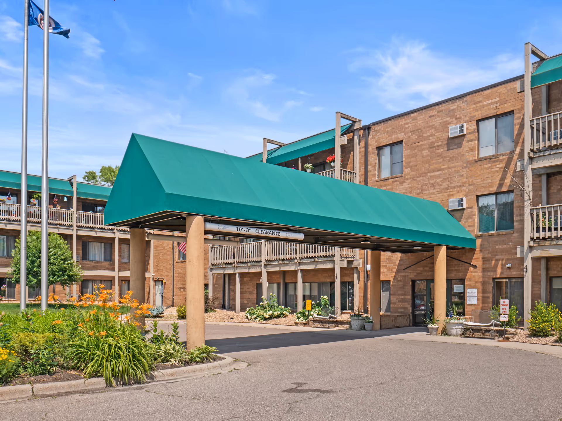 Brick senior living building with a green canopy over the entrance and landscaped courtyard.