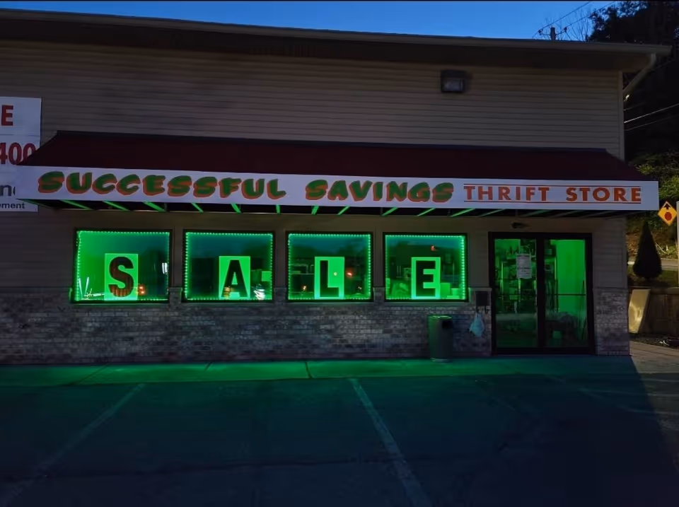 Front of a thrift store with neon green windows spelling 'SALE' and a red canopy.