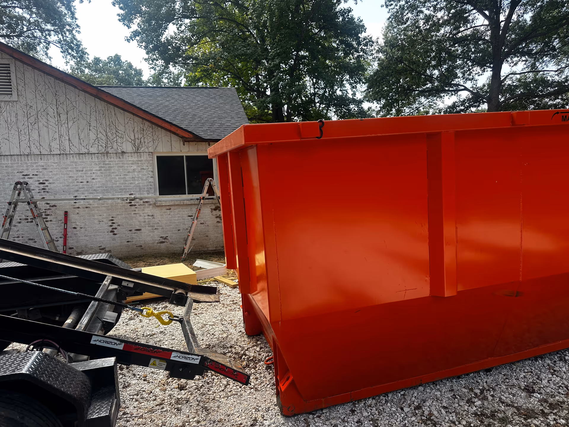 A large orange dumpster and construction debris sit outside a brick building.