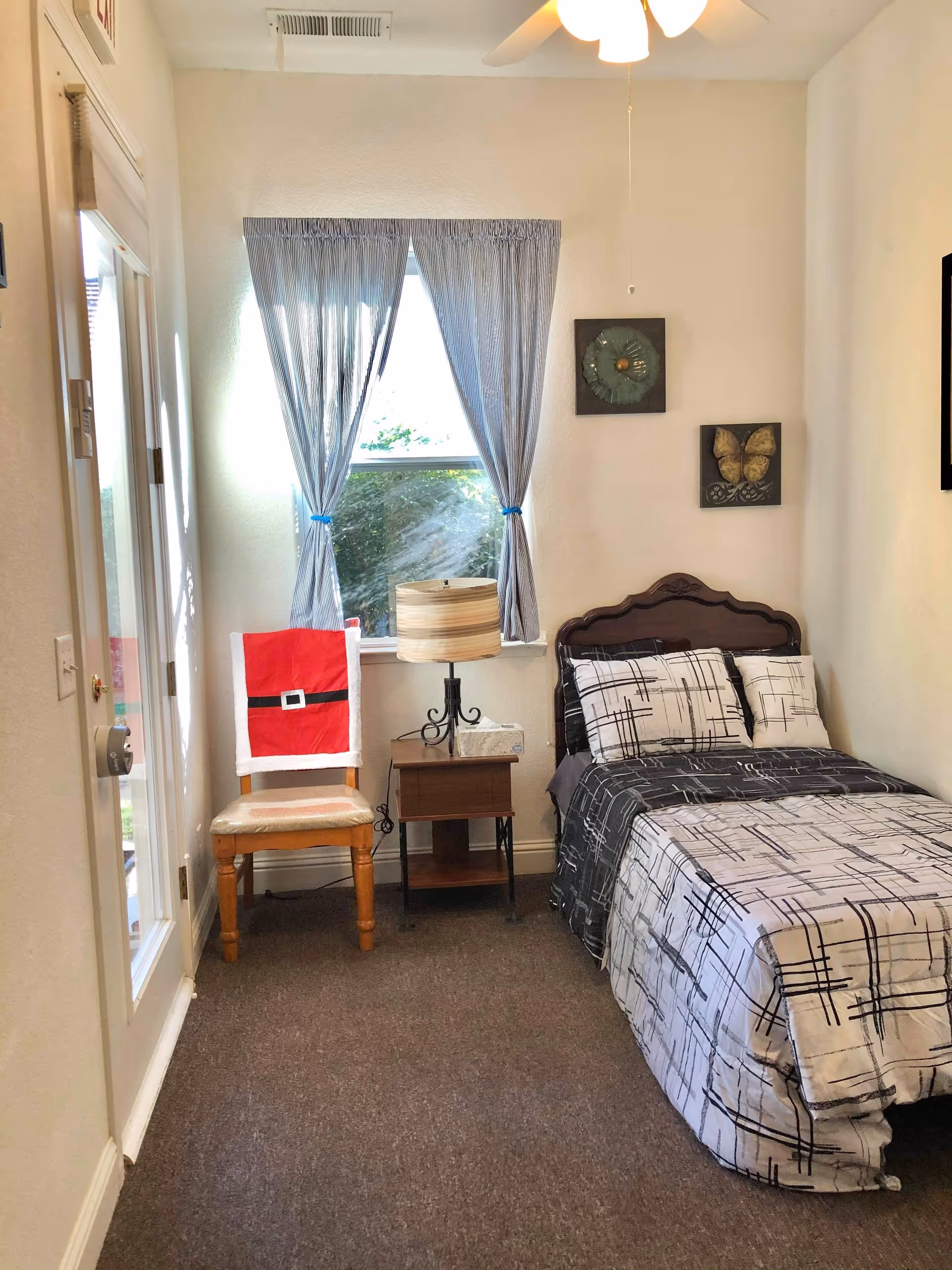 Small bedroom with a single bed, bedside table and lamp next to a window with tied-back curtains.