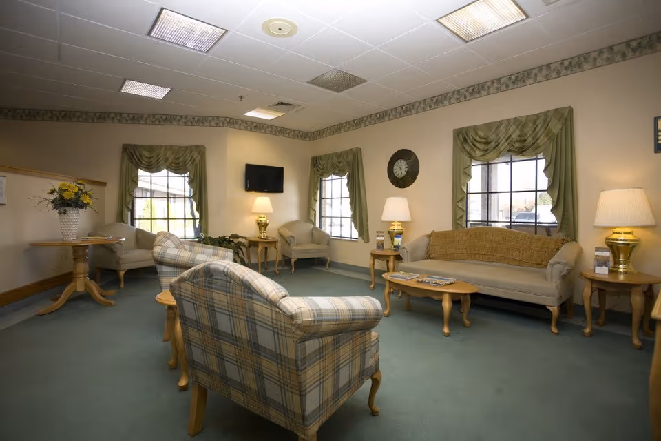 Senior living lounge with plaid chair, sofa, coffee tables, and lamps.