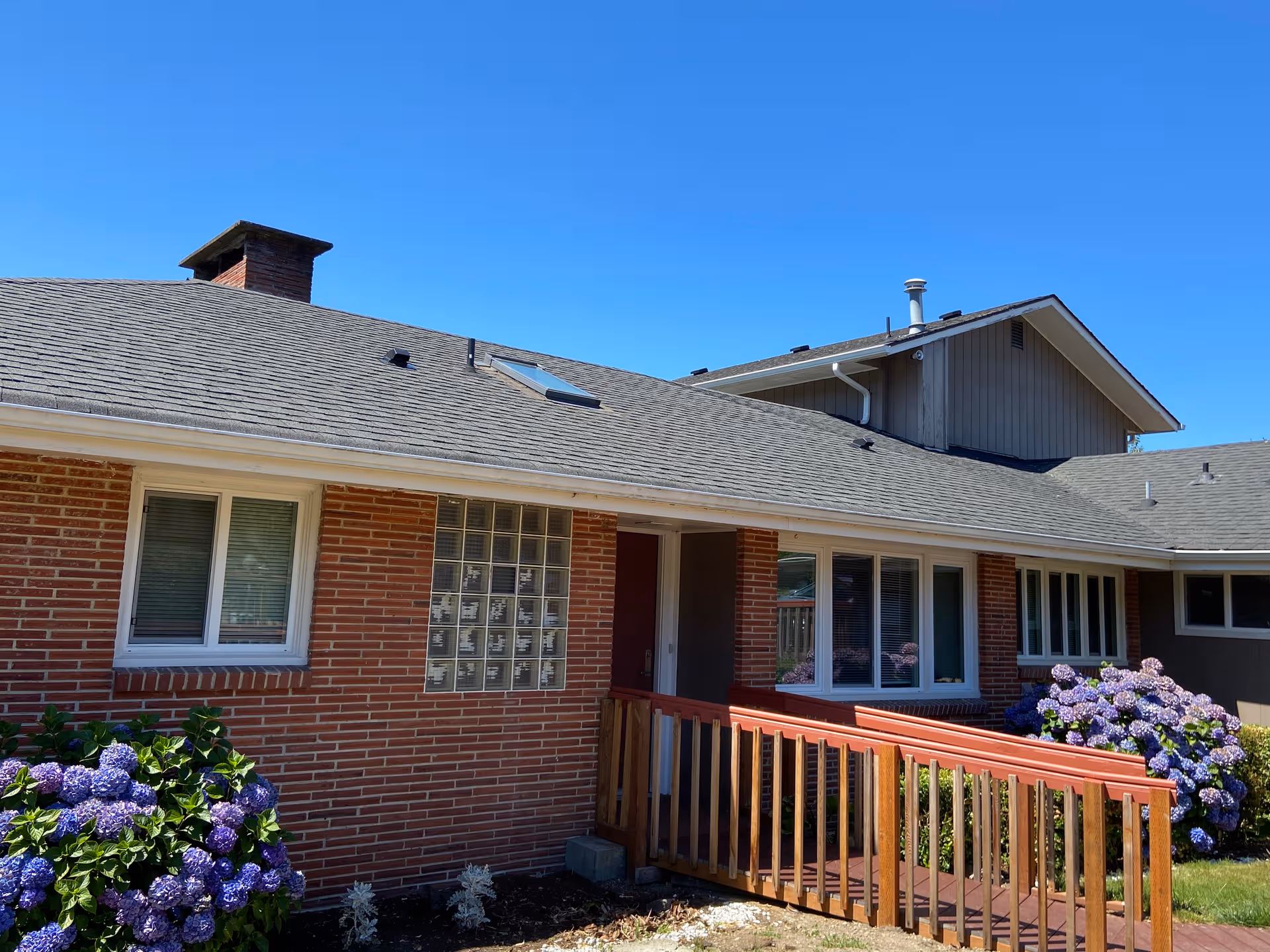 Brick senior living facility with wooden ramp, blooming hydrangeas, and clear blue sky.