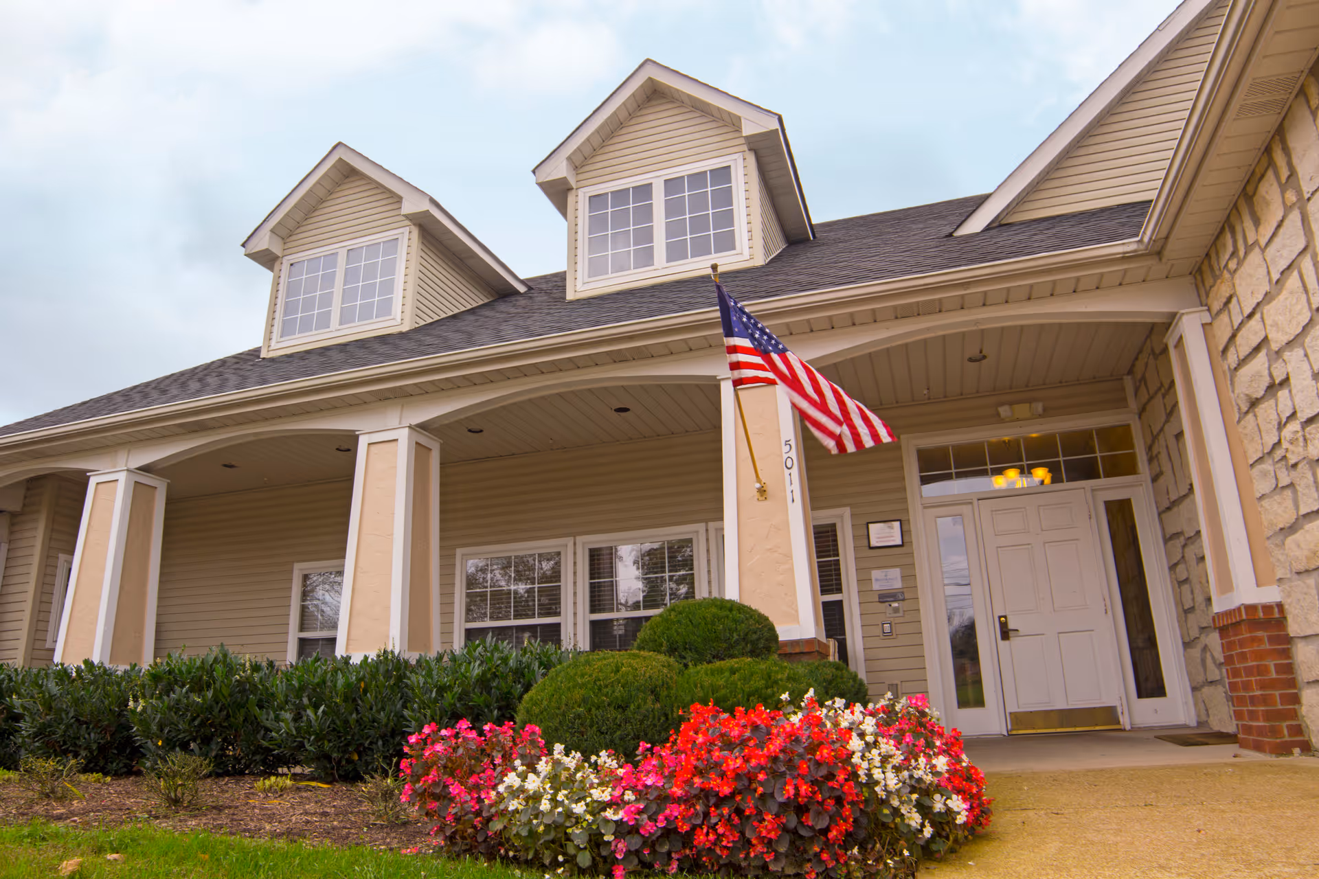 Front view of Brookdale Columbia facility with entrance, flag, and vibrant flower bed.