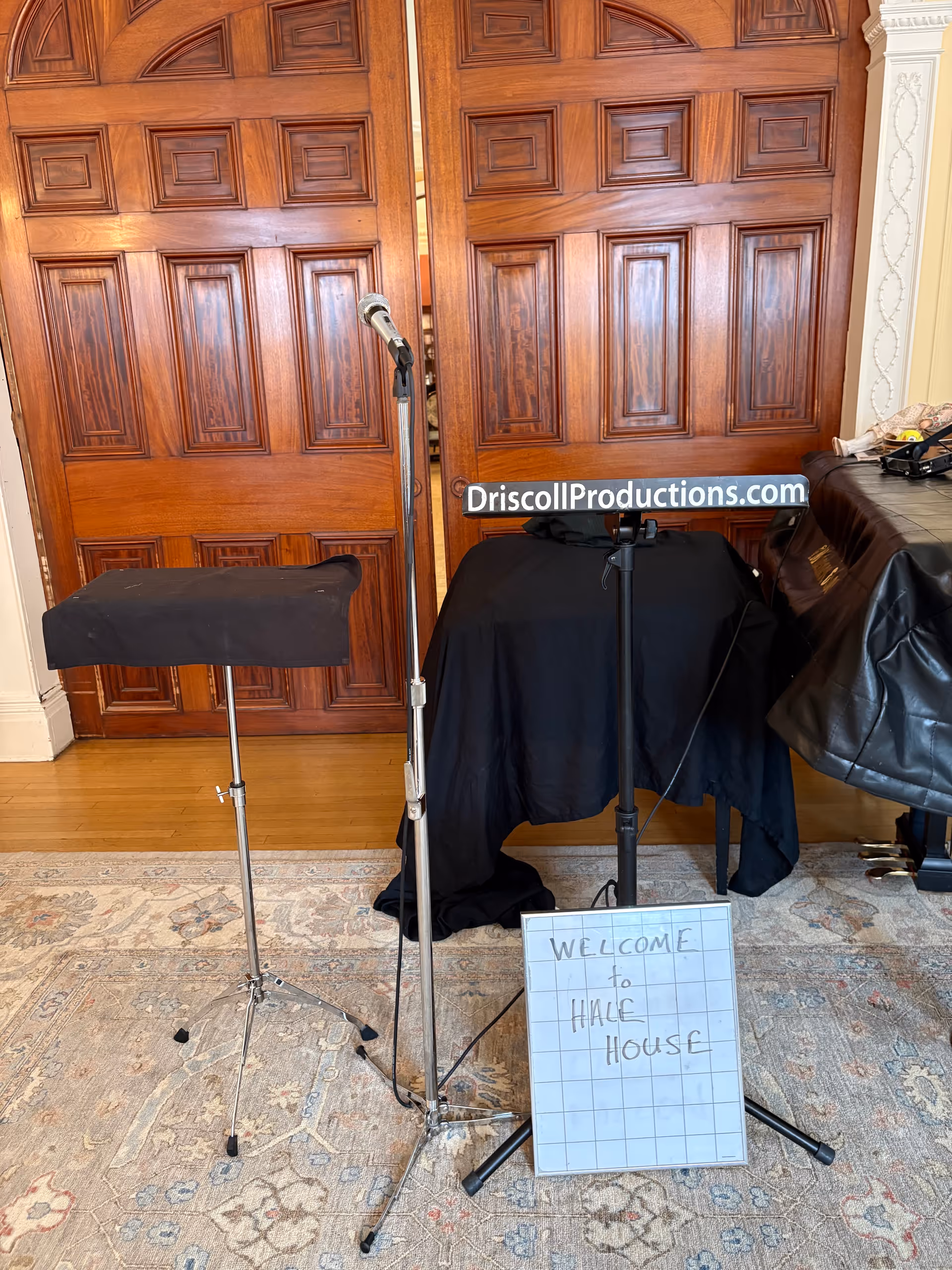 Interior scene showing microphone stand, table with black cloth, and a Welcome to Hale House sign.
