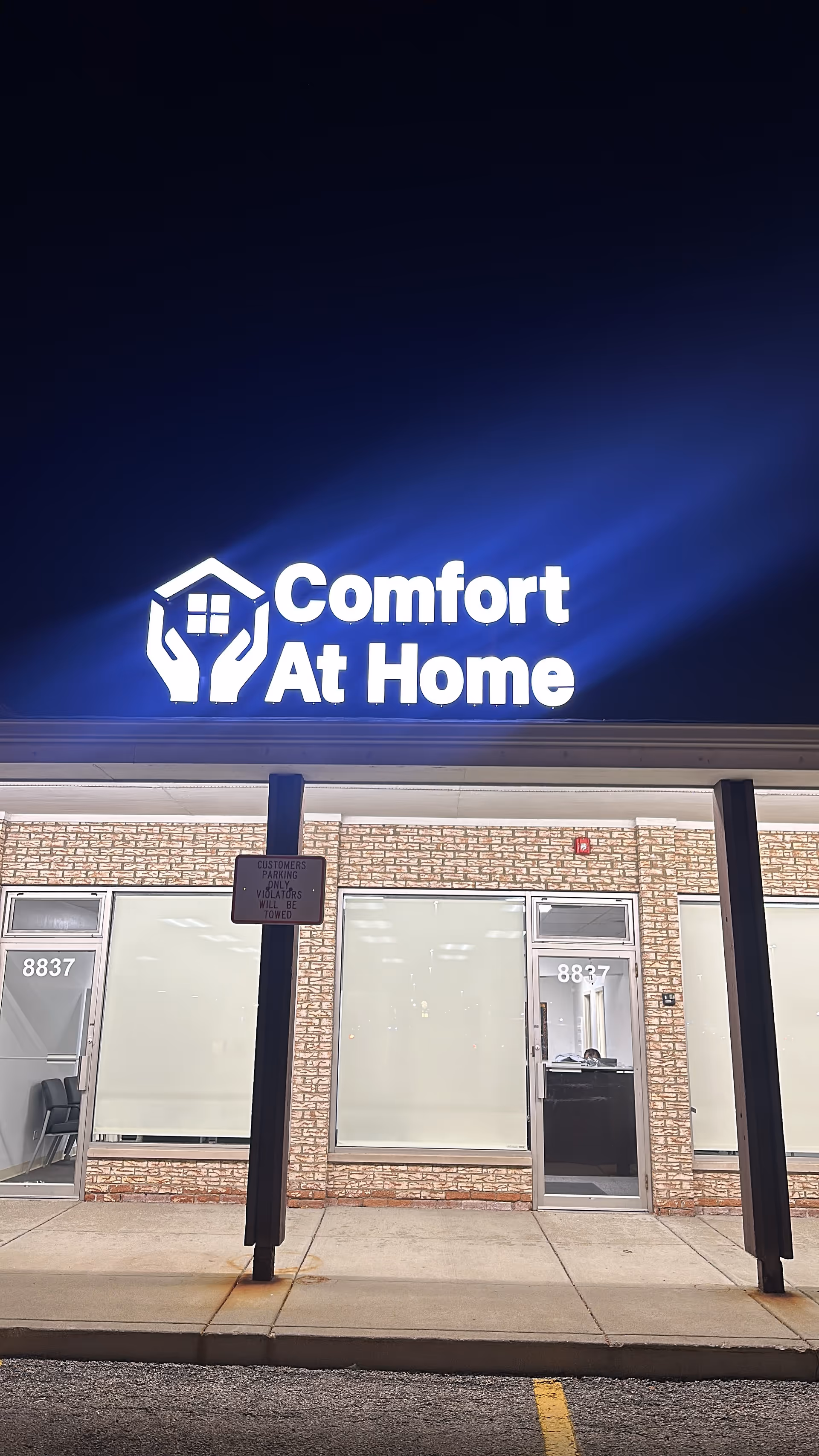 Exterior storefront with Comfort At Home sign above brick building and glass doors