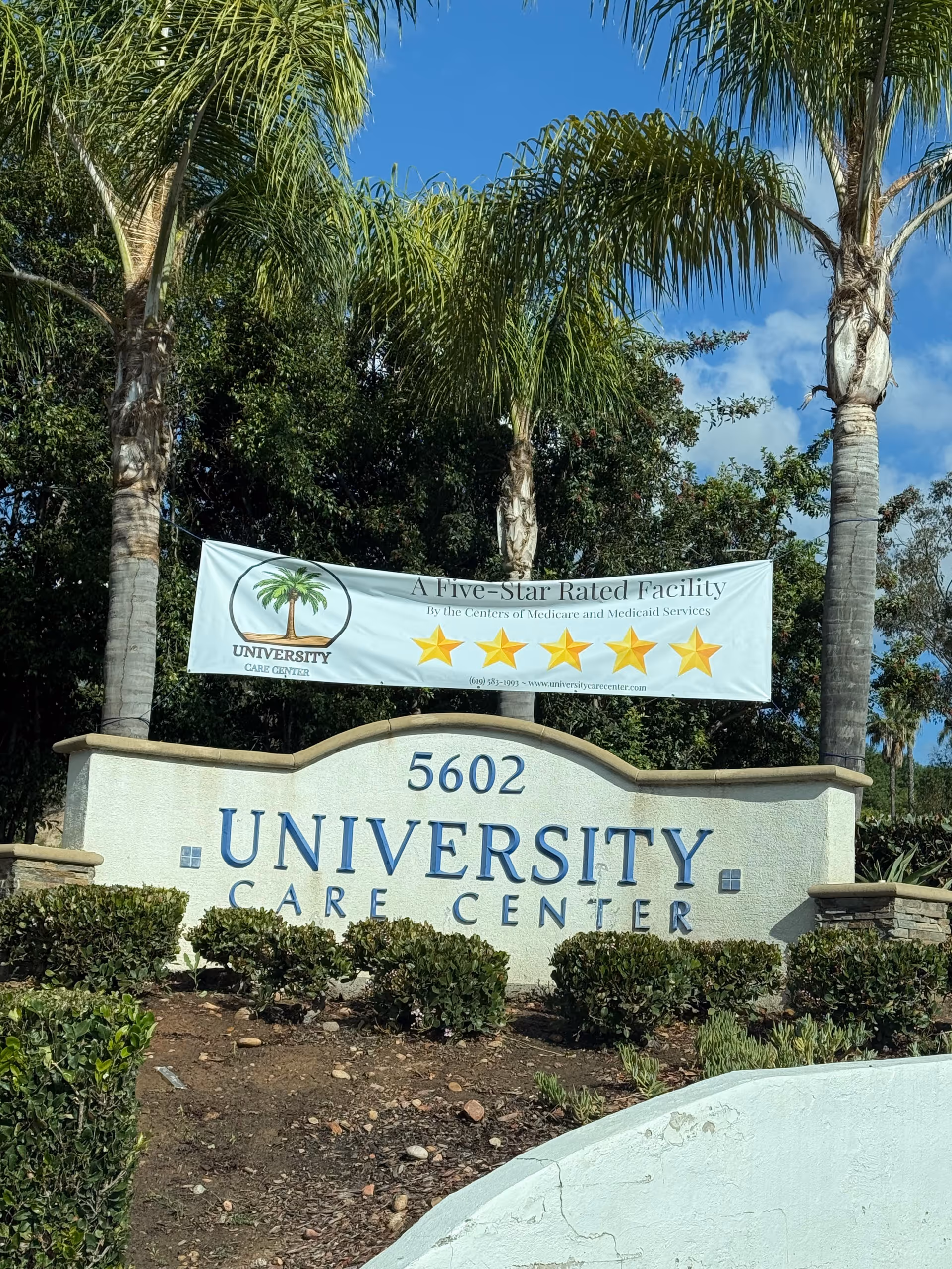 Exterior view of a University Care Center sign with palm trees and a banner.