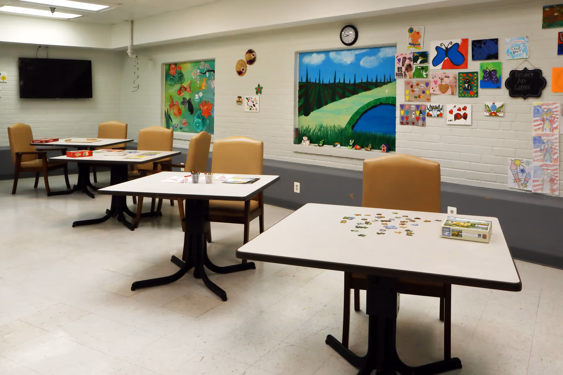 Interior dining area with several tables, beige chairs, and colorful wall art.