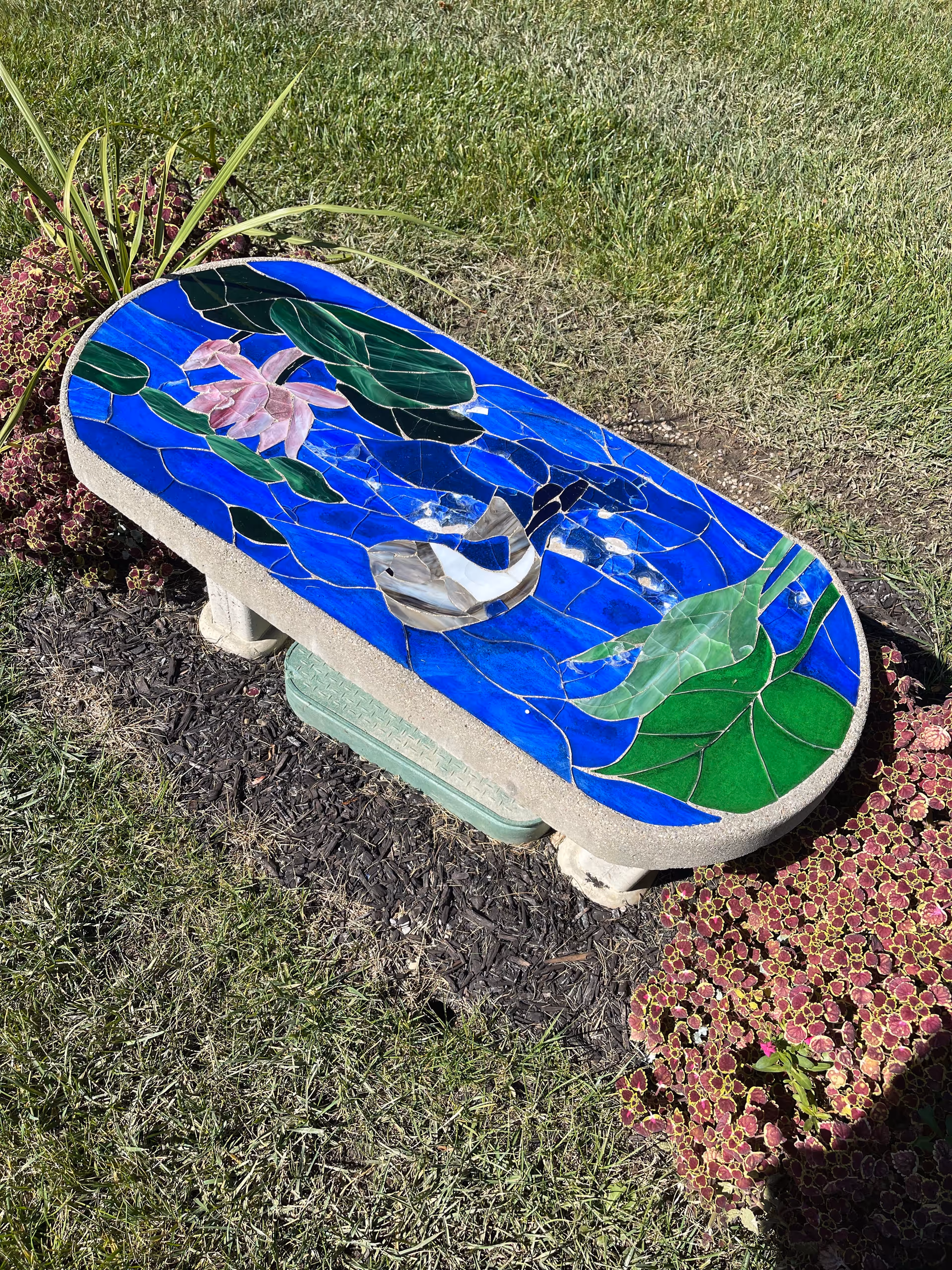 Outdoor mosaic bench with blue and green tiles on a grassy lawn.