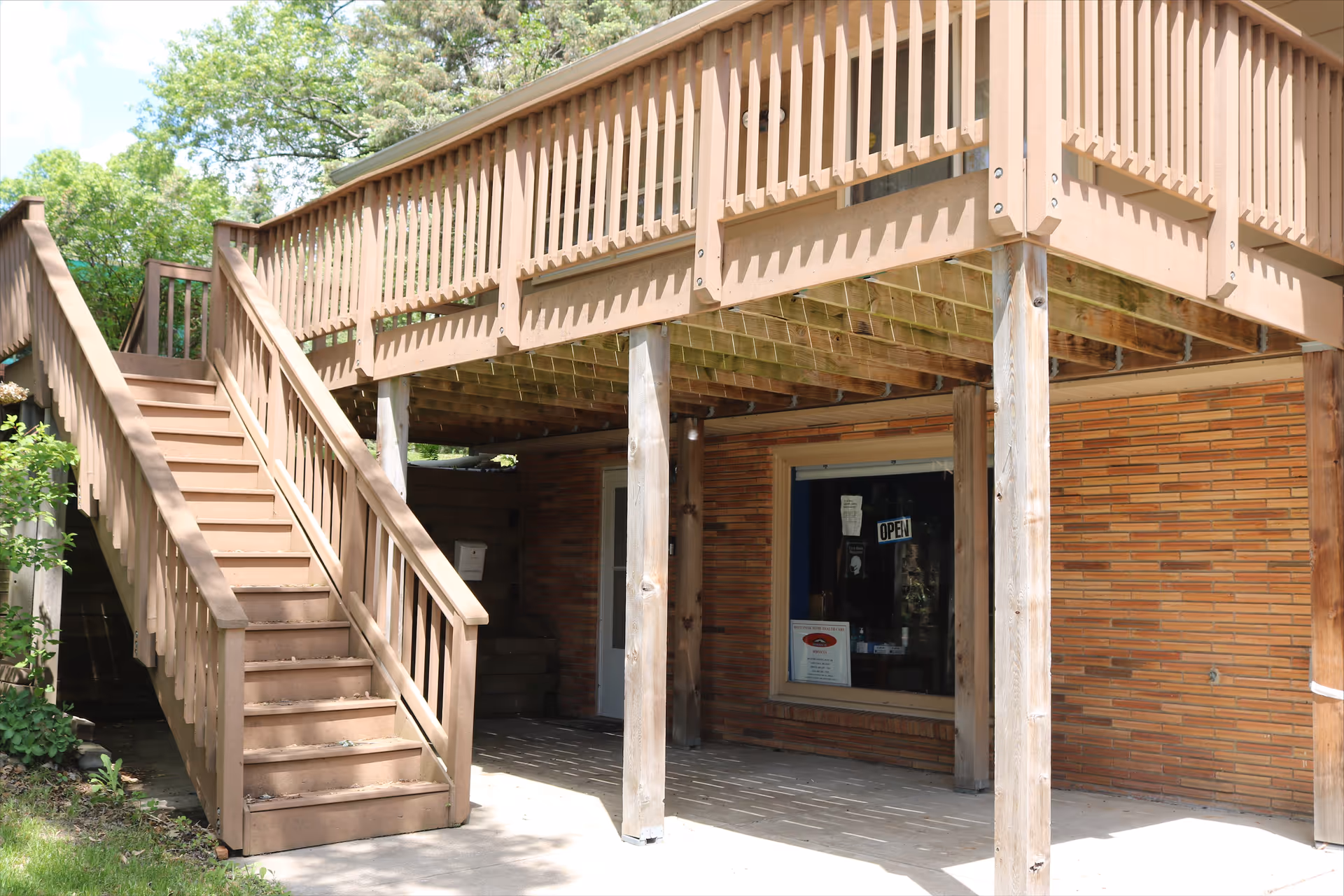 Wooden elevated exterior deck with stairs attached to a brick building's front entrance.