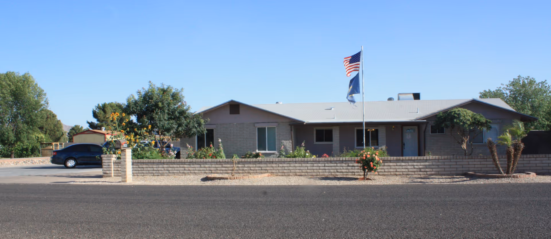Single-story facility with flagpole displaying two flags, brick front, landscaping, and a parked car.