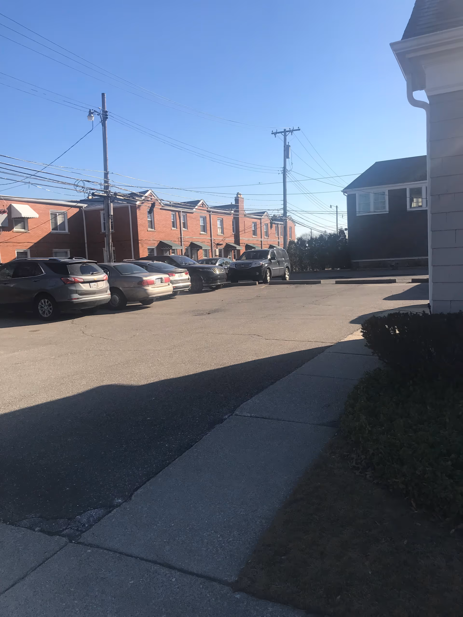 Parking lot in front of a building, with cars, power lines, and blue sky.