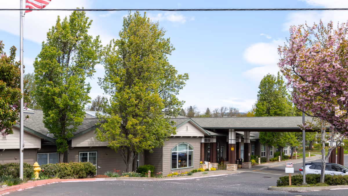 Providence Brookside Manor exterior: single-story building with trees, a covered entrance, and a parked car.