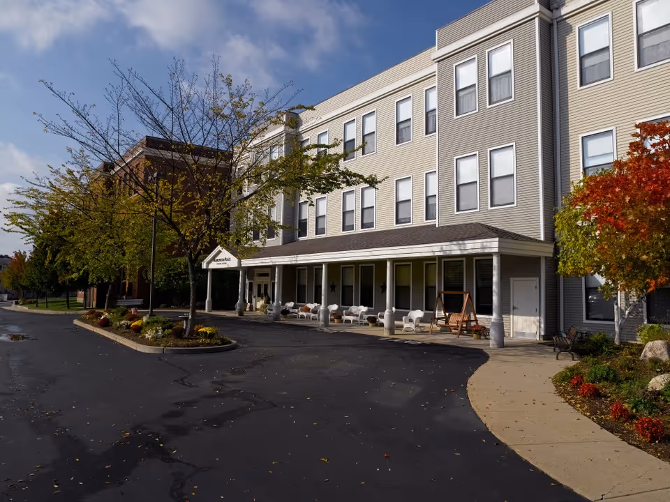 Three-story residential building with a covered porch, outdoor seating and a curved driveway surrounded by autumn trees.