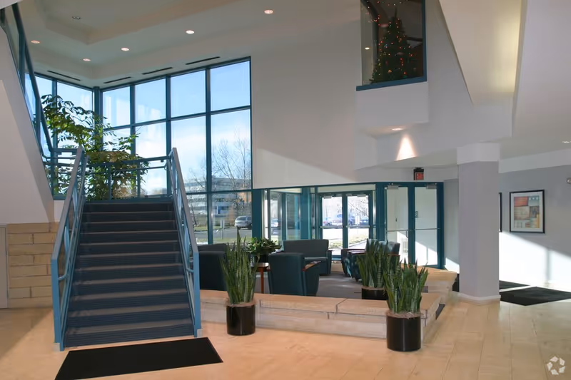 Bright modern facility lobby with stairs, seating area, plants, and large glass entrance.