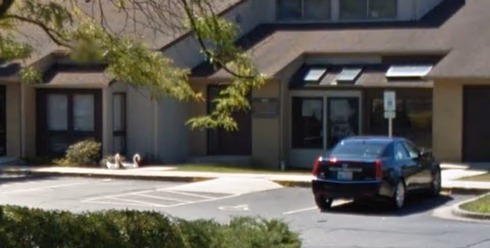 Exterior view of a senior living facility with a parking lot and car.