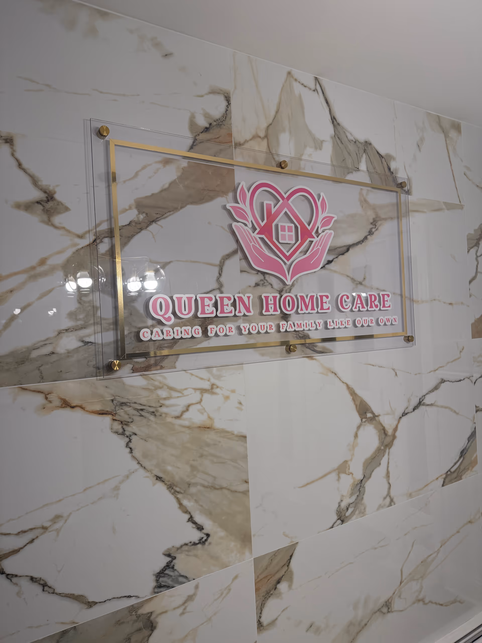 Indoor marble wall displays a pink Queen Home Care sign and logo.