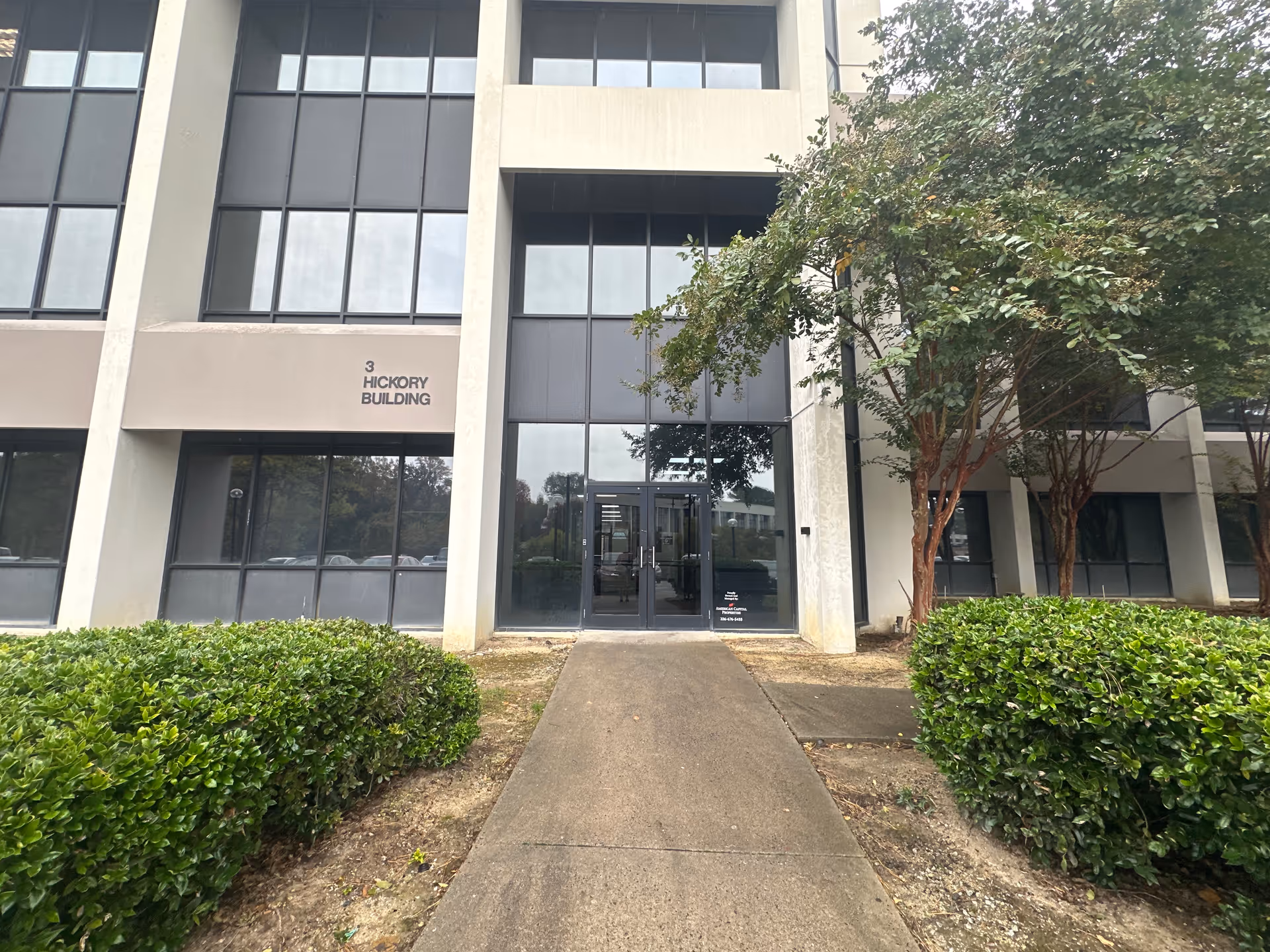 Entrance to Hickory Building with large glass doors, concrete path, and shrubs.