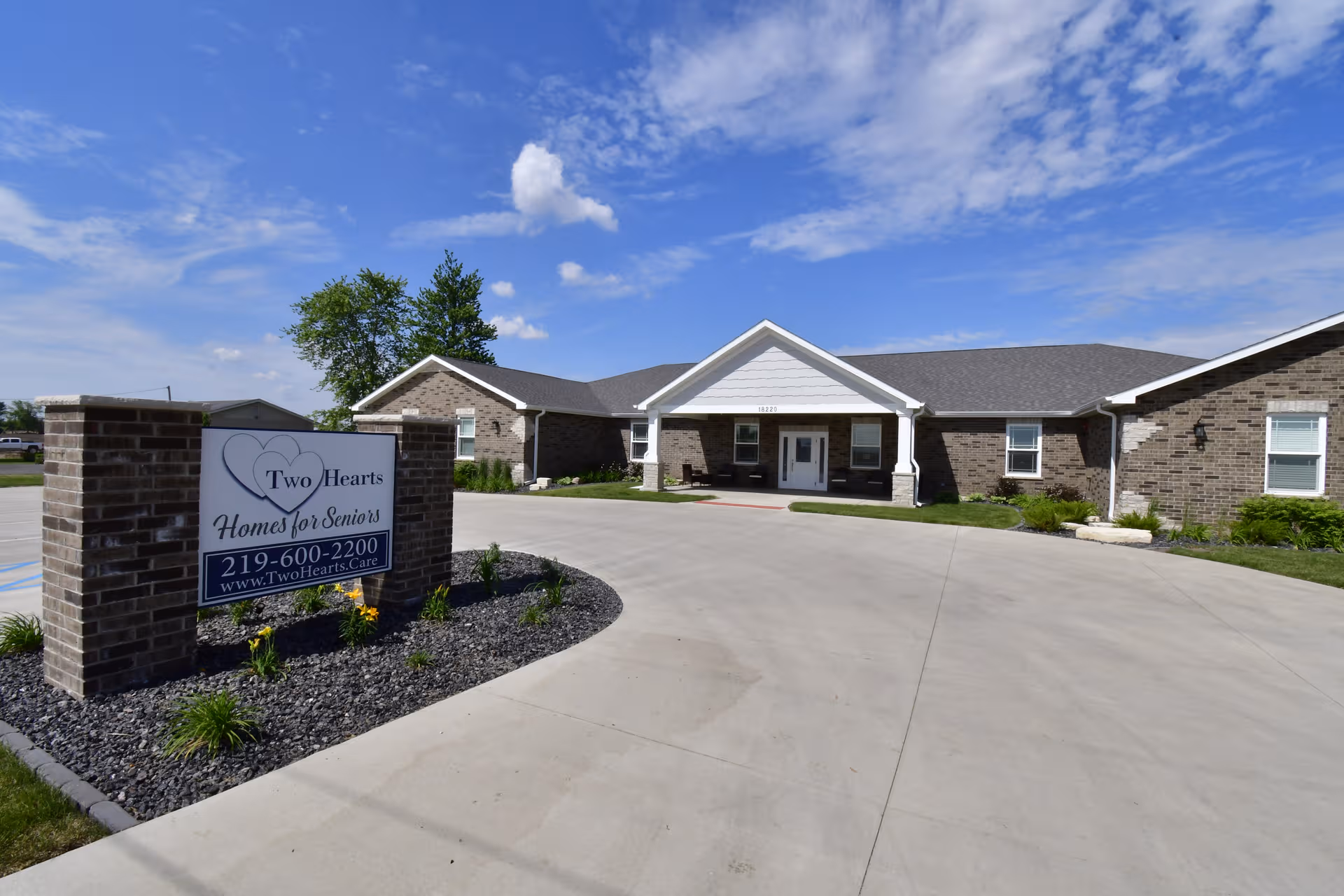 Brick senior residence with curved driveway and sign reading Two Hearts Homes for Seniors.