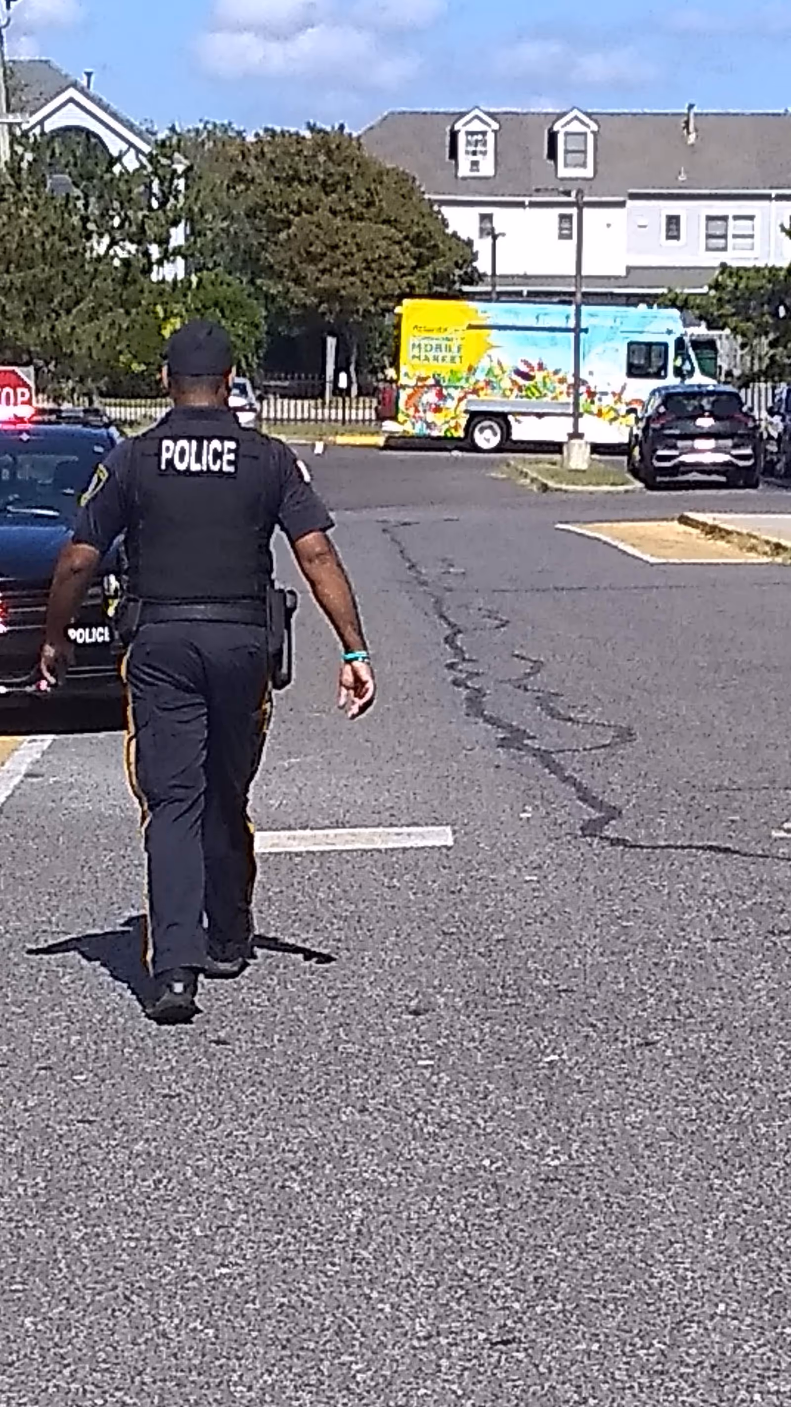 A police officer walks away across a parking lot toward a colorful market truck.