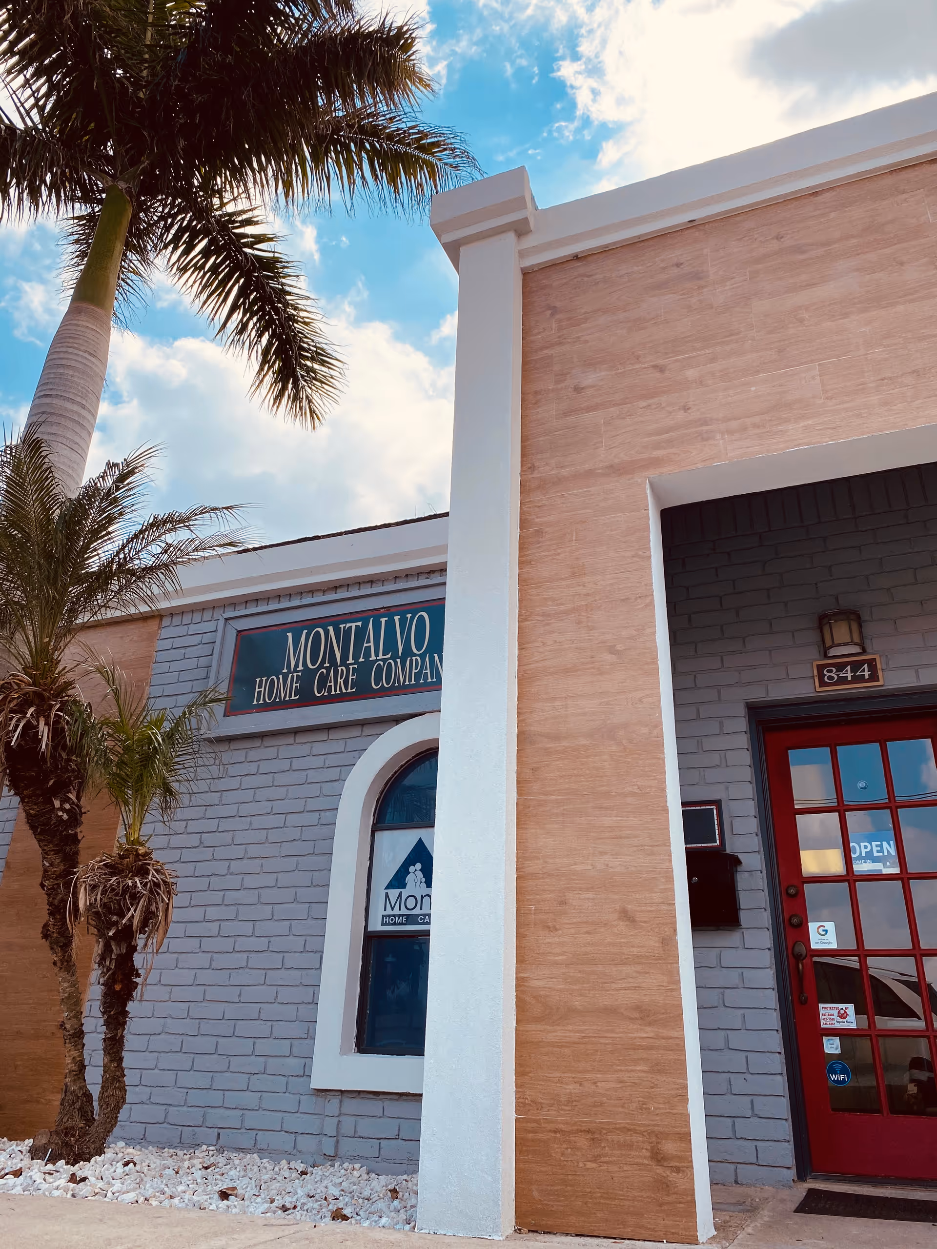 Exterior view of Montalvo Home Care Co. entrance with palm trees and blue sky.