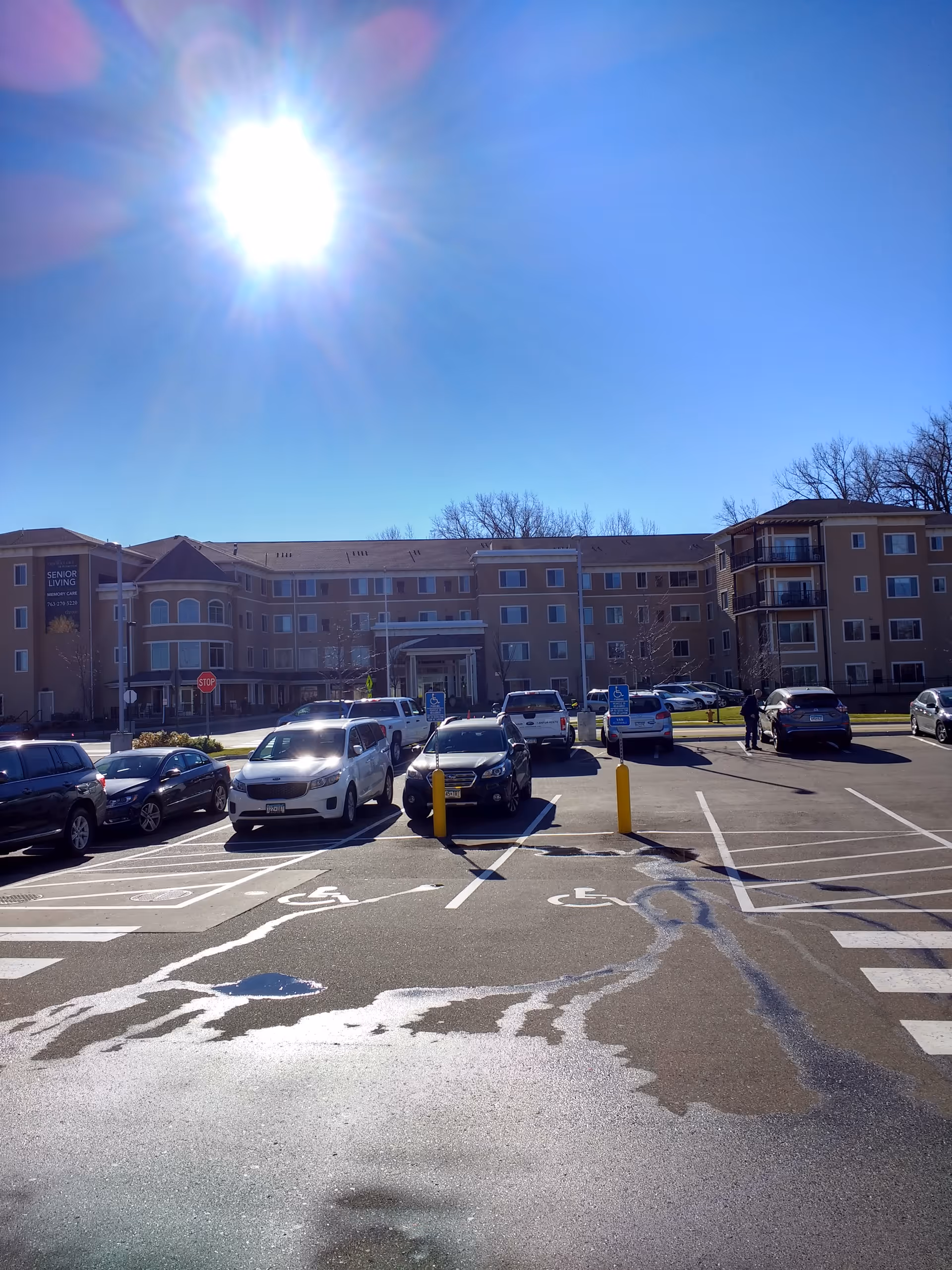 Sunlit exterior of The Waters of Plymouth with a parking lot and cars.