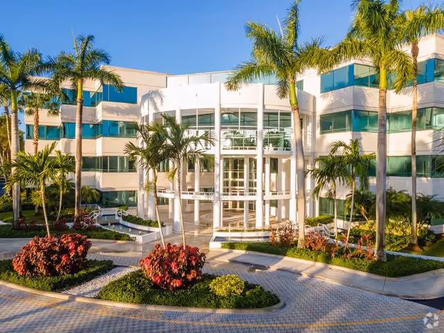 Modern senior living building entrance surrounded by palm trees and landscaped walkways.