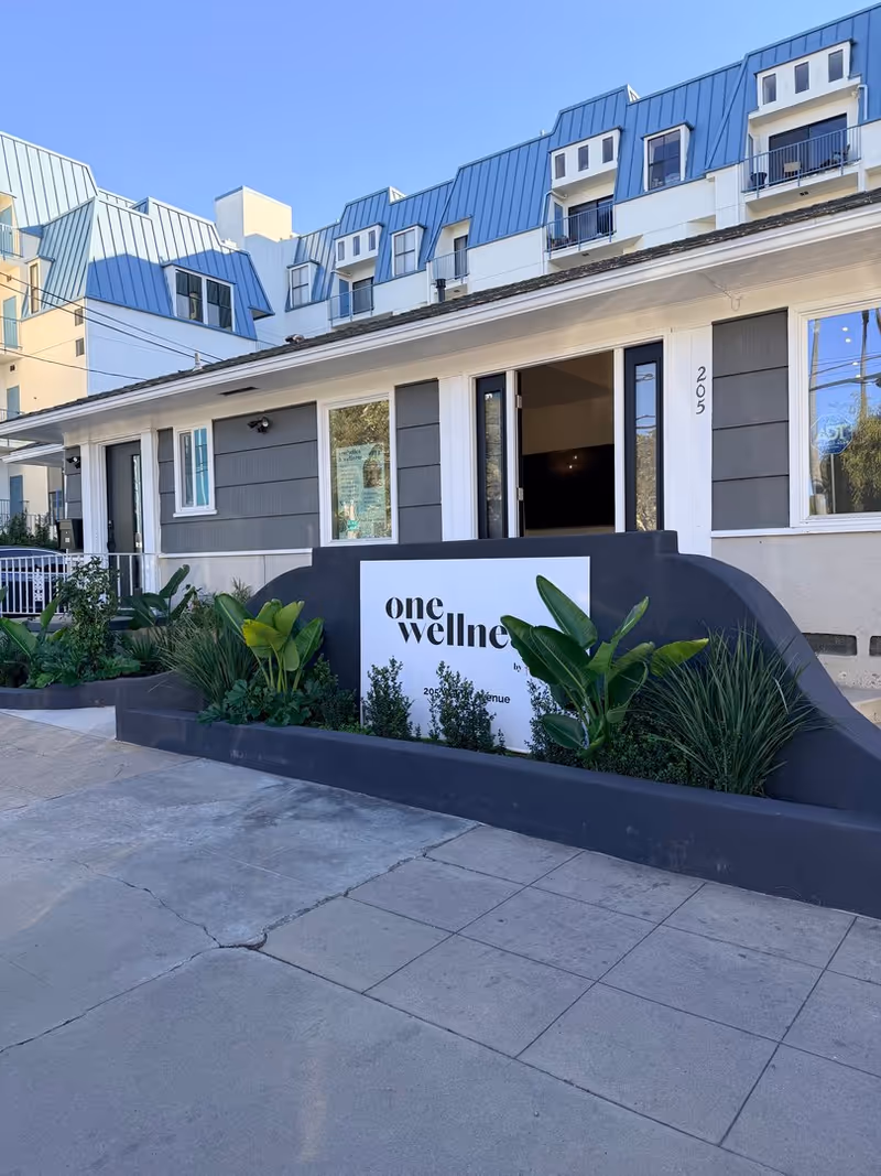 Exterior view of a building entrance with a curved sign and tropical plants.