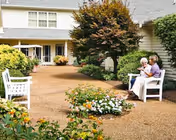 Outdoor courtyard at Southern Oaks Assisted Living with gravel path, flower beds, and residents seated.