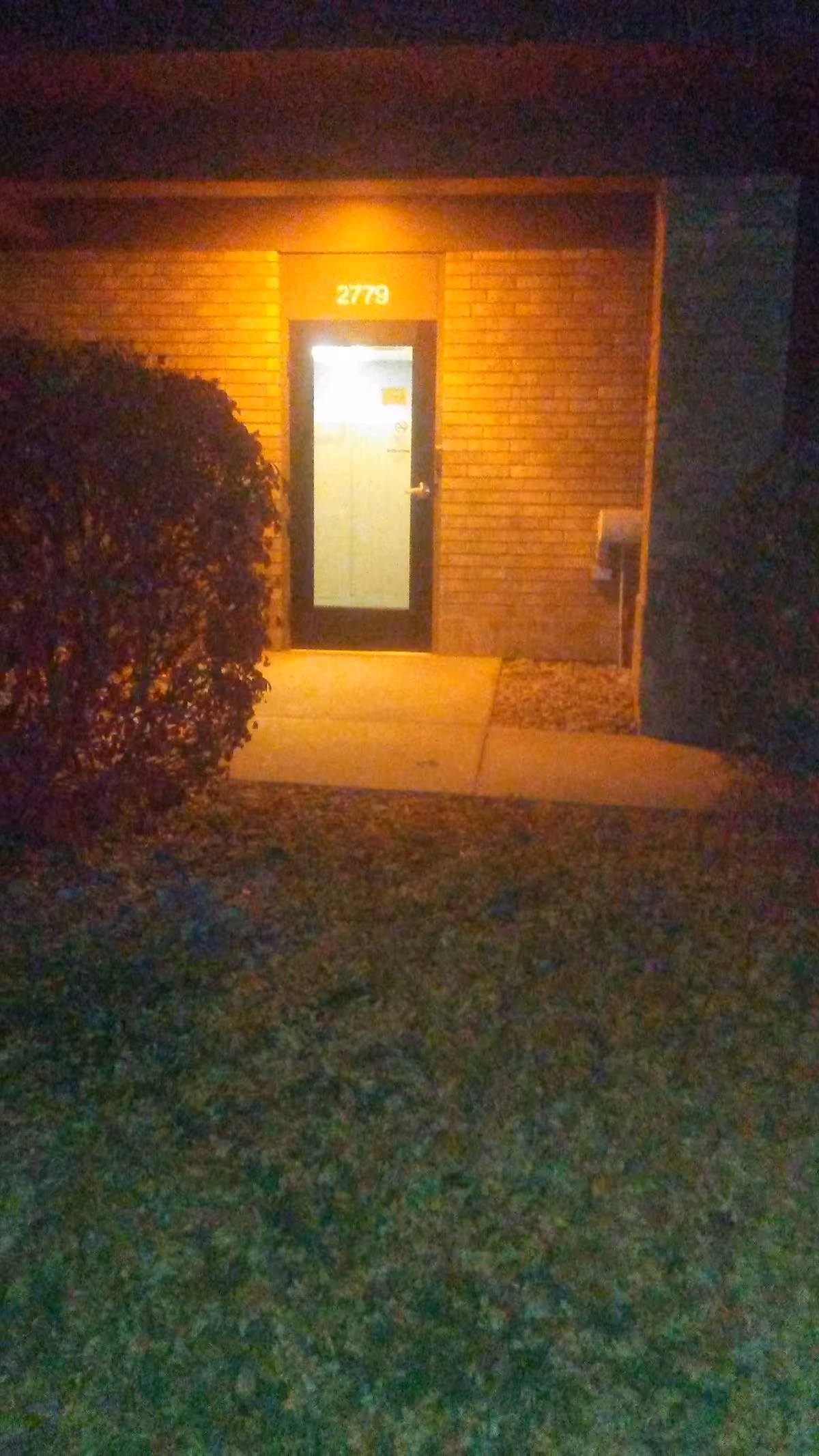 Night exterior view of brick building entrance with illuminated door and address 2779
